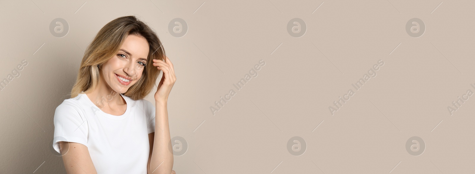 Photo of Portrait of happy young woman with beautiful blonde hair and charming smile on beige background