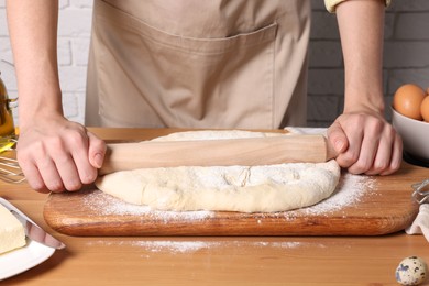 Photo of Woman rolling dough with wooden pin at table near white brick wall, closeup