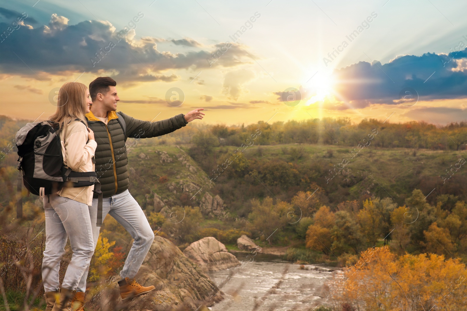 Photo of Couple of hikers with travel backpacks enjoying beautiful view near mountain river