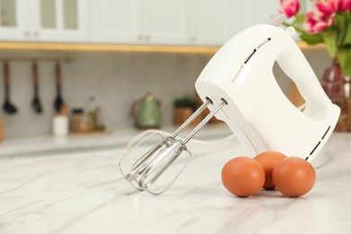 Photo of Modern mixer and eggs on white marble table in kitchen, space for text