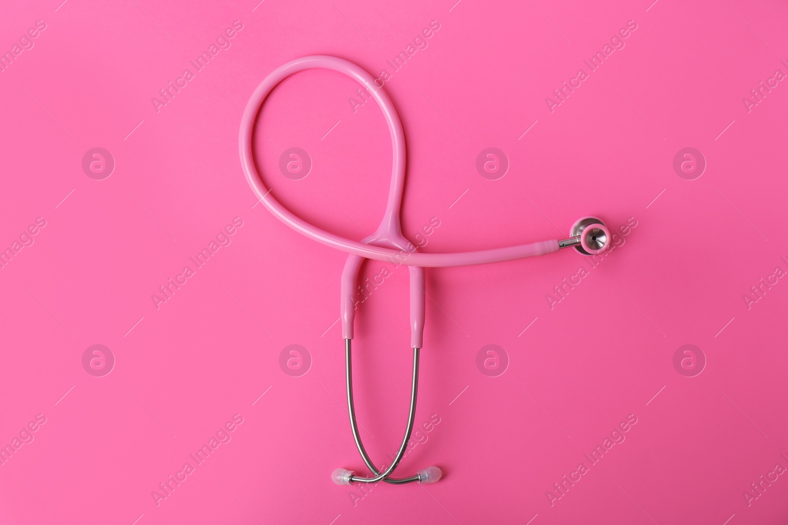 Photo of Pink stethoscope as awareness ribbon on color background, top view. Breast cancer concept