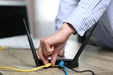 Photo of Woman inserting ethernet cable into Wi-Fi router at table indoors, closeup