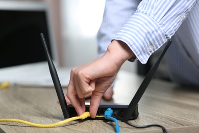 Woman inserting ethernet cable into Wi-Fi router at table indoors, closeup