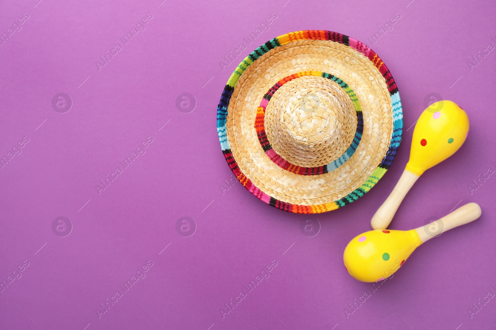 Photo of Mexican sombrero hat and maracas on purple background, flat lay. Space for text