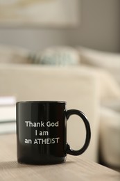 Cup with phrase Thank God I Am Atheist on wooden table