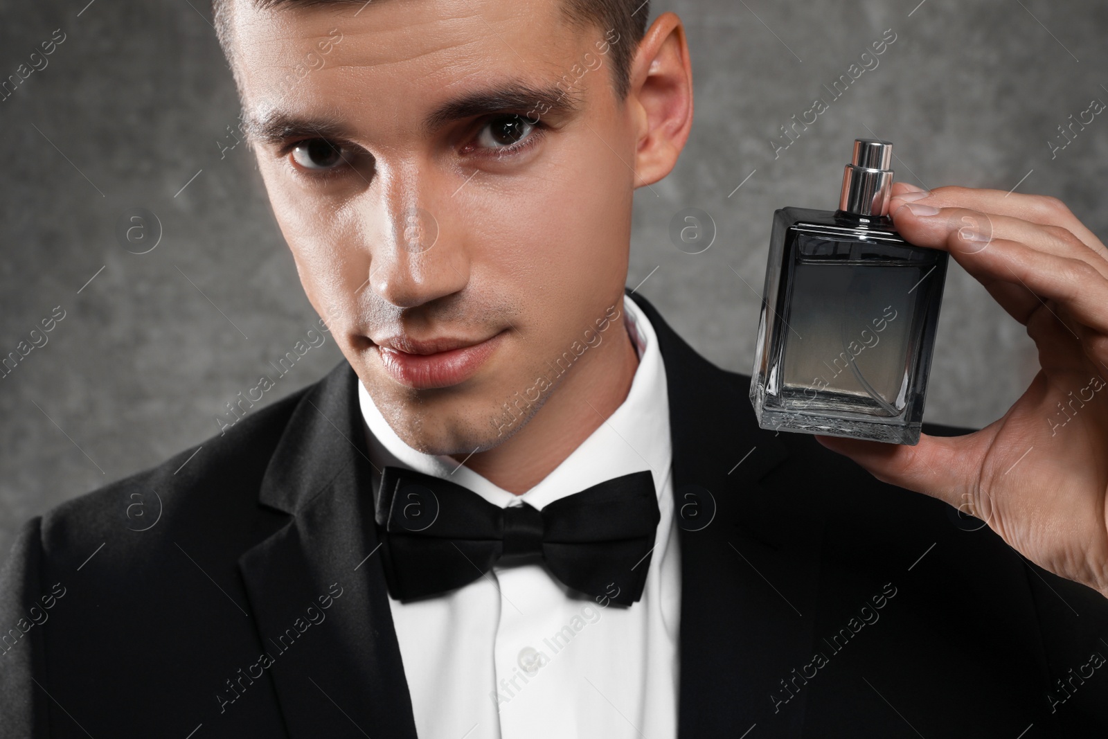 Photo of Handsome young man with bottle of perfume on grey stone background