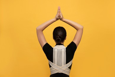 Woman with orthopedic corset on orange background, back view