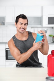 Young athletic man with protein shake powder in kitchen