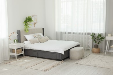 Stylish bedroom interior with large comfortable bed, ottoman and bedside table