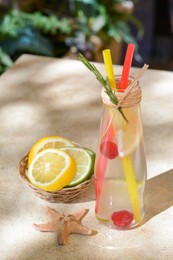Photo of Refreshing tasty lemonade served in glass bottle and citrus fruits on beige table