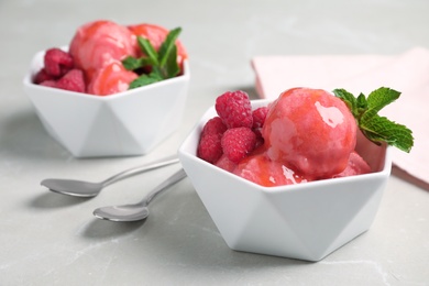 Photo of Delicious pink ice cream with raspberries and mint in bowls on grey marble table