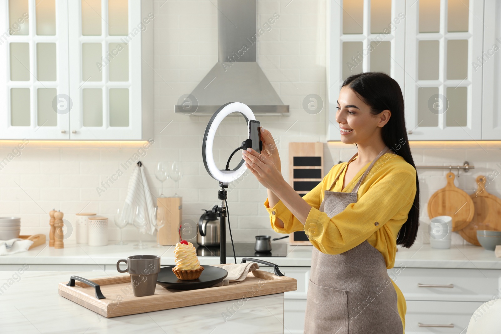 Photo of Blogger preparing for video recording in kitchen at home. Using smartphone and ring lamp