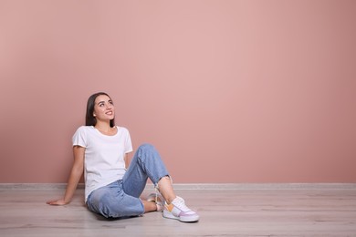 Photo of Young woman sitting on floor near pink wall indoors. Space for text