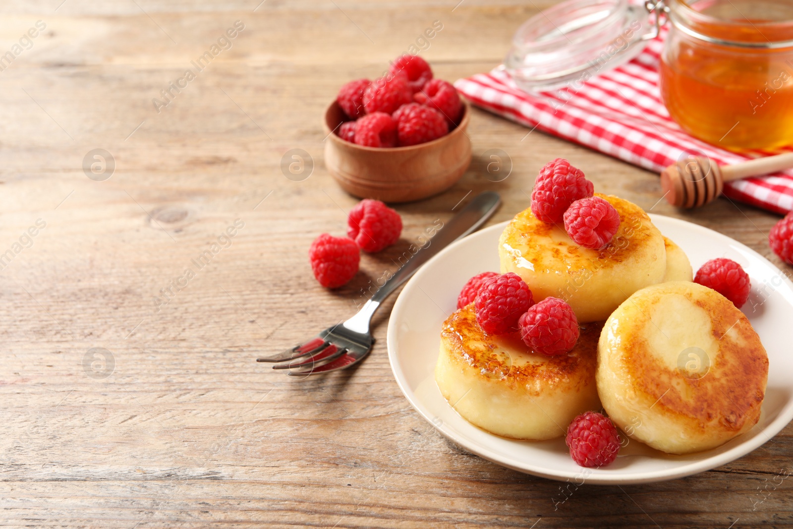 Photo of Delicious cottage cheese pancakes with raspberries on wooden table. Space for text