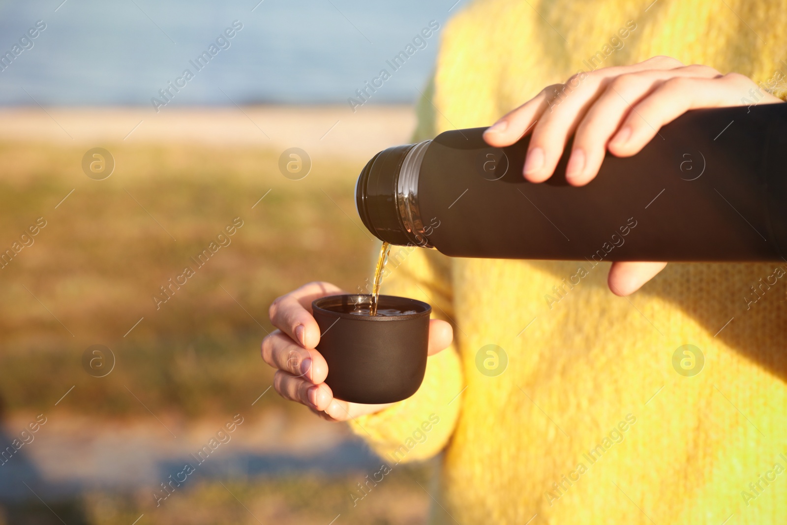 Photo of Woman pouring hot drink from thermos into cap outdoors, closeup