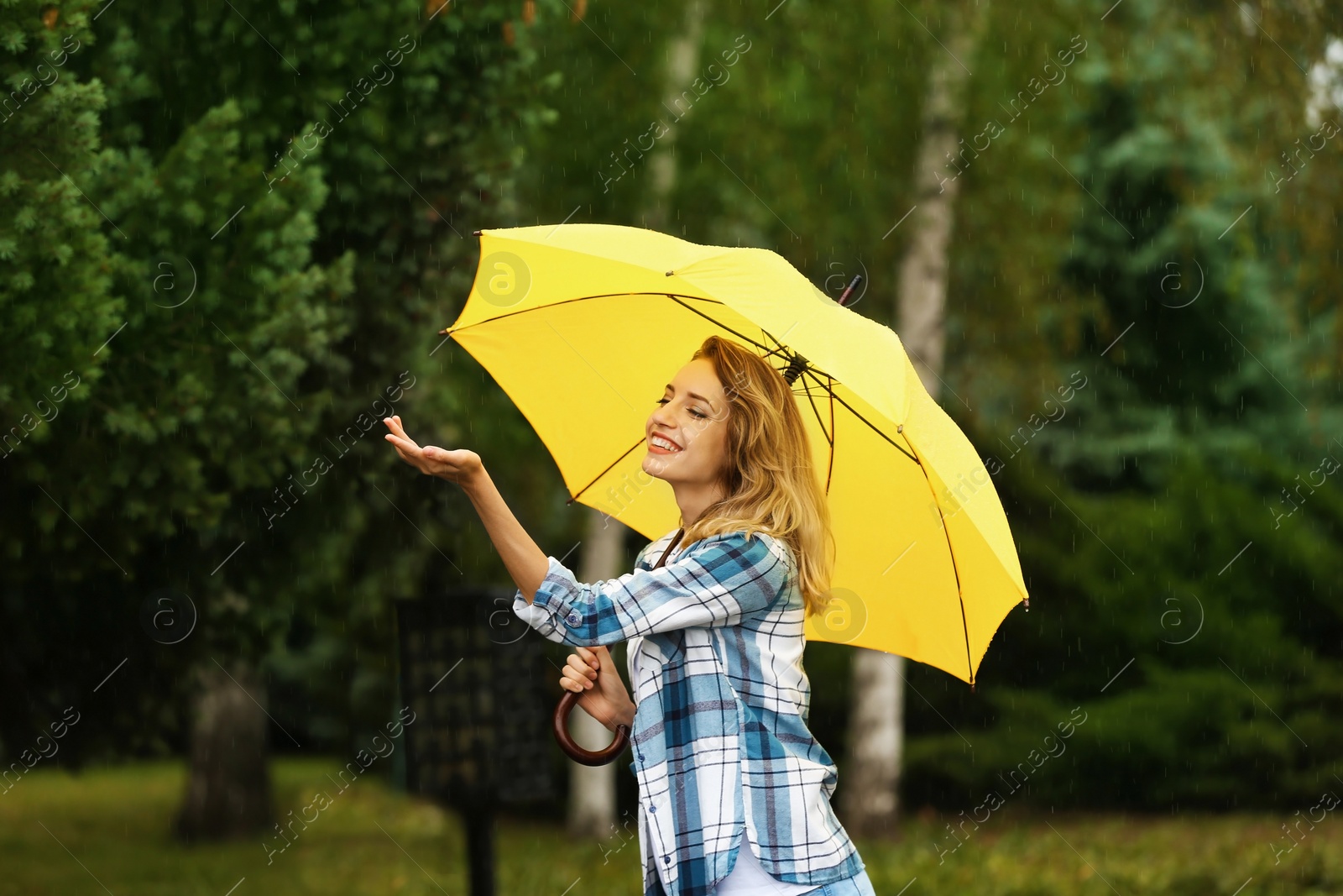 Photo of Happy young woman with umbrella under rain in park