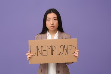 Photo of Asian woman holding sign with word Unemployed on purple background