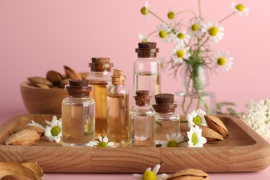 Aromatherapy. Different essential oils, flowers and almonds on pink background