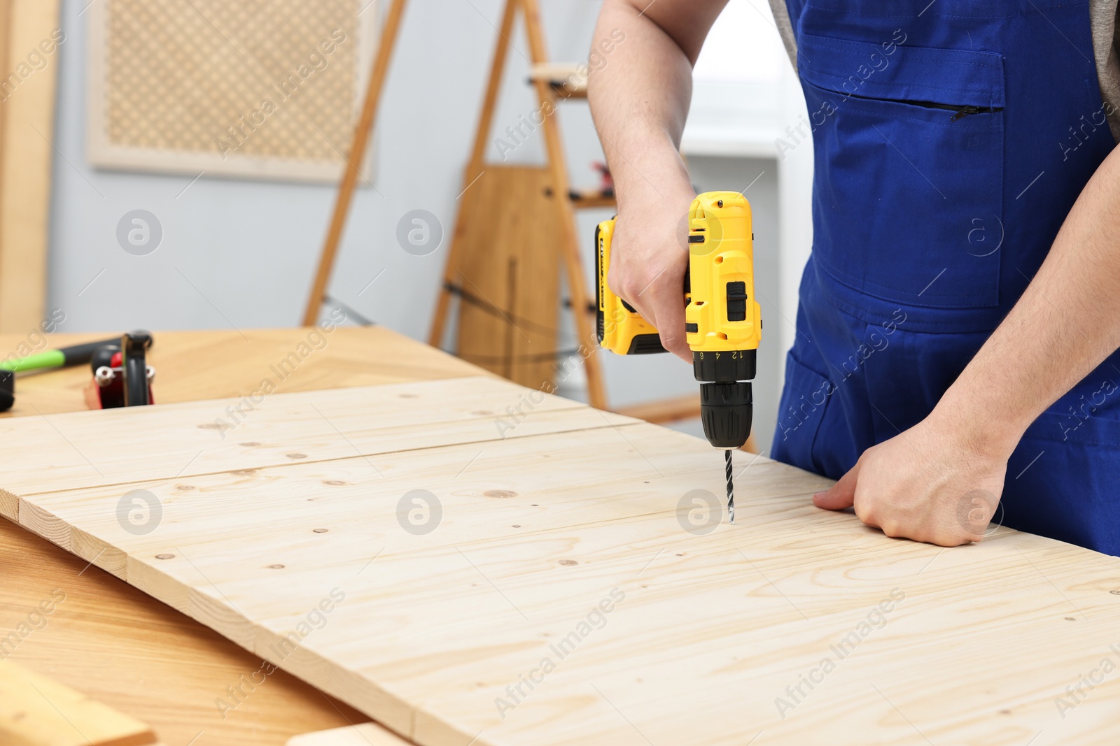 Photo of Young worker using electric drill at table in workshop, closeup