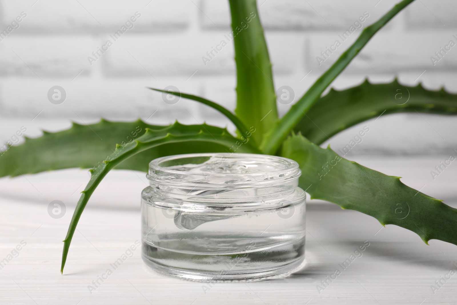 Photo of Jar of cosmetic gel and aloe vera leaves on white wooden table, closeup