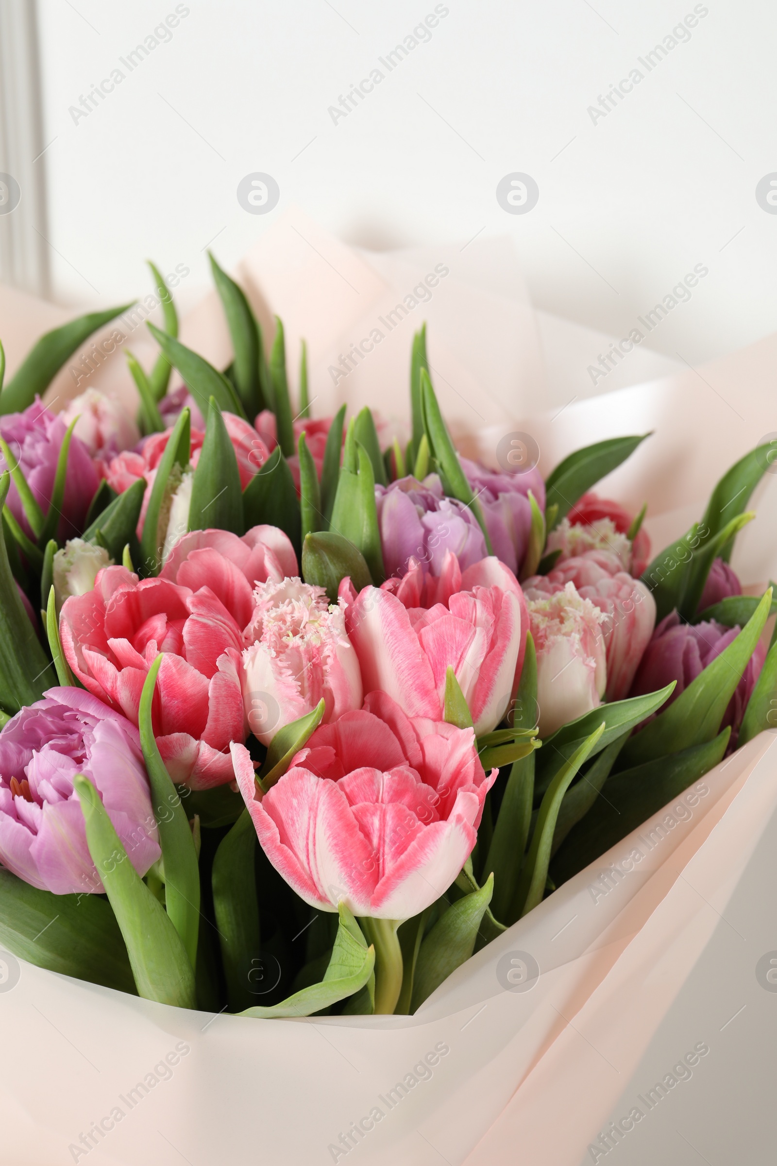 Photo of Bouquet of beautiful tulips near white wall, closeup