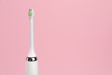 Photo of Electric toothbrush on pink background, space for text