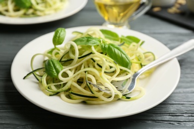 Photo of Delicious zucchini pasta with basil served on grey wooden table, closeup