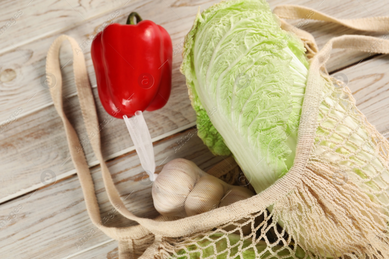 Photo of Fresh Chinese cabbage, bell pepper and garlic in net bag on wooden table, closeup