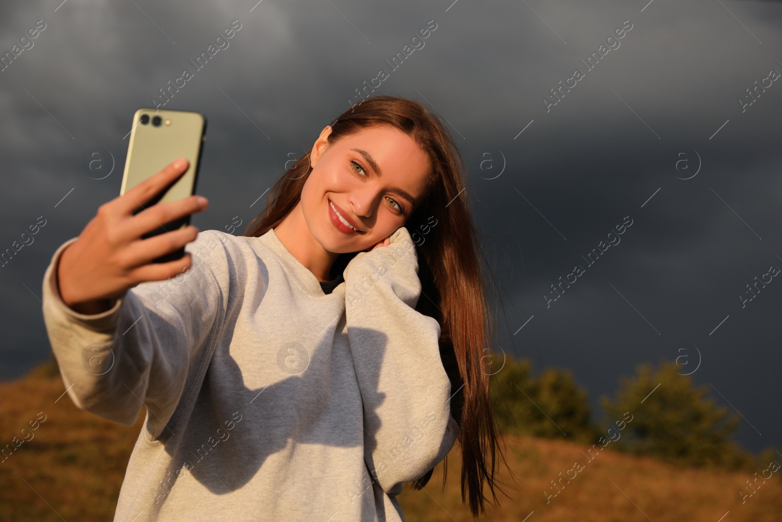 Photo of Young woman taking selfie against rainy clouds