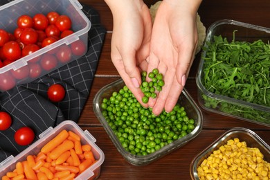 Woman putting green peas into glass container at wooden table, above view. Food storage