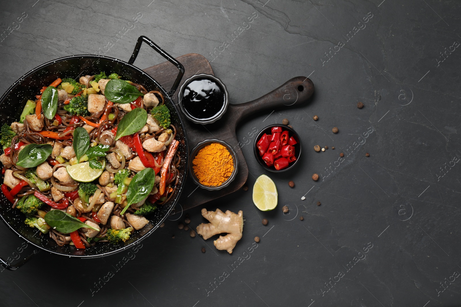 Photo of Stir-fry. Tasty noodles with meat in wok and ingredients on grey textured table, flat lay