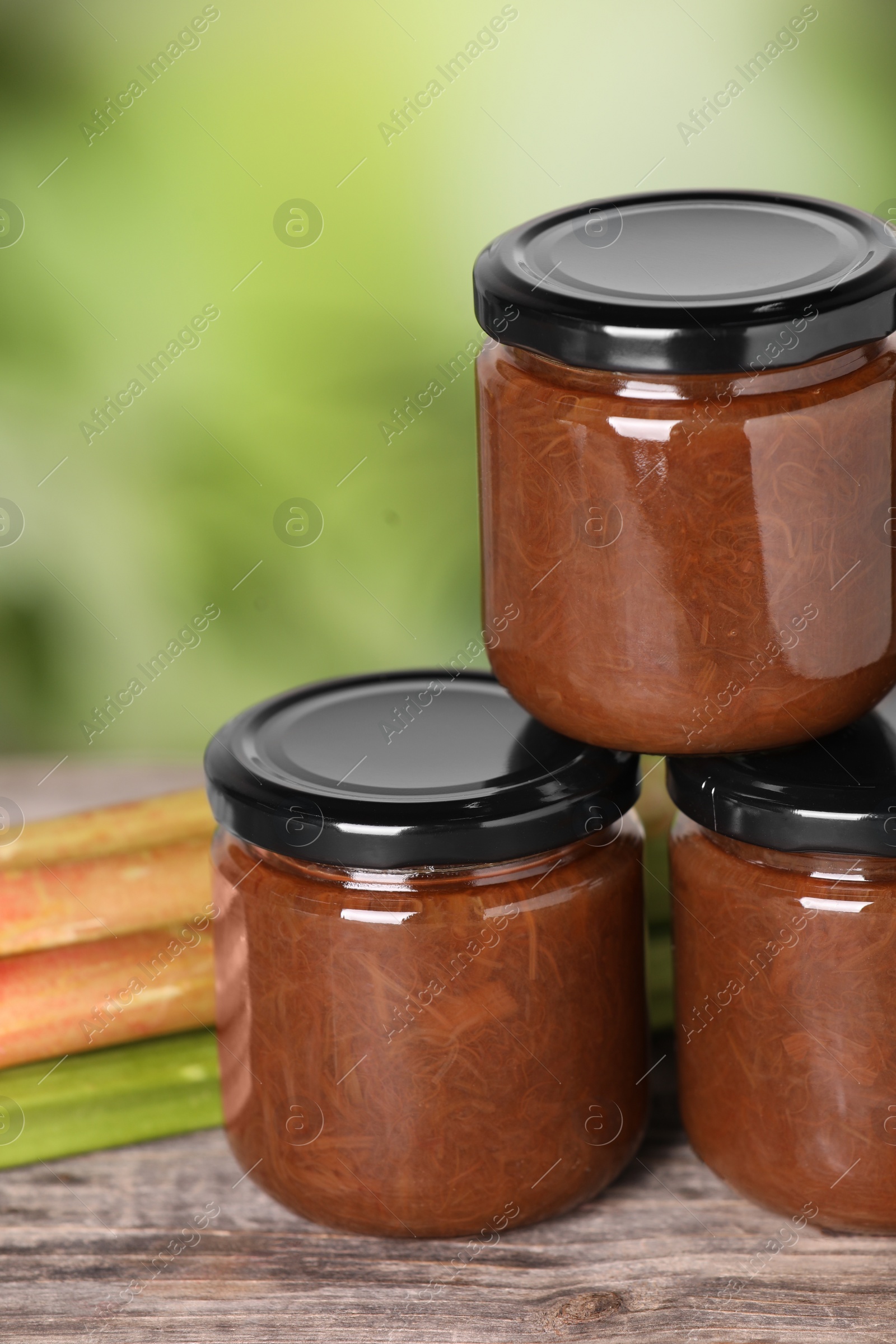 Photo of Jars of tasty rhubarb jam on wooden table, closeup