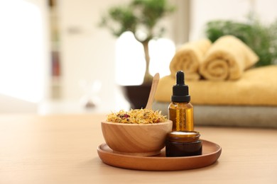 Photo of Bottle of essential oil, dry flowers and jar with cream on light wooden table, space for text. Spa therapy