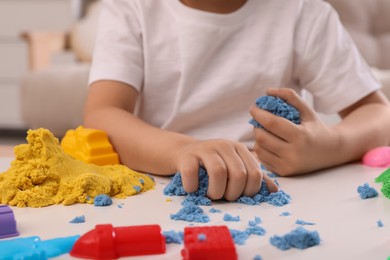 Photo of Little boy playing with bright kinetic sand at table indoors, closeup