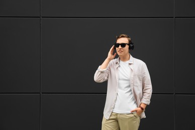 Photo of Handsome young man with headphones near black wall. Space for text