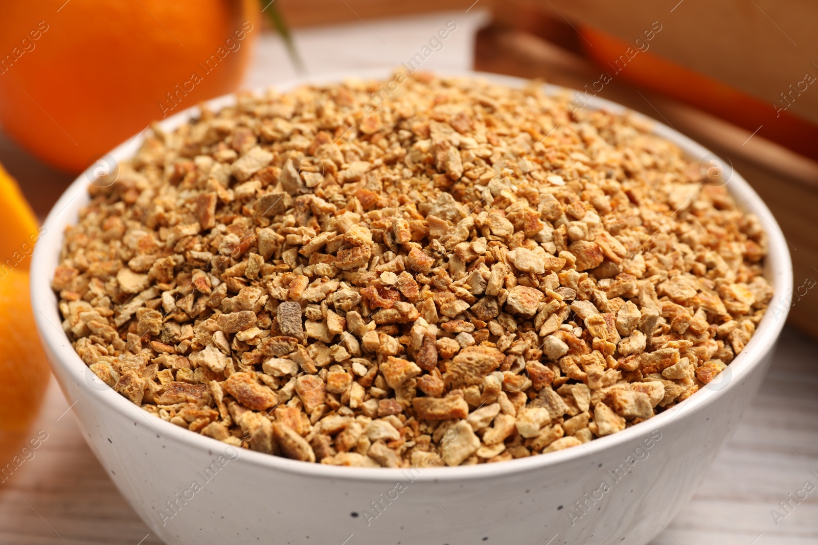 Photo of Bowl with dried orange seasoning zest on white wooden table, closeup