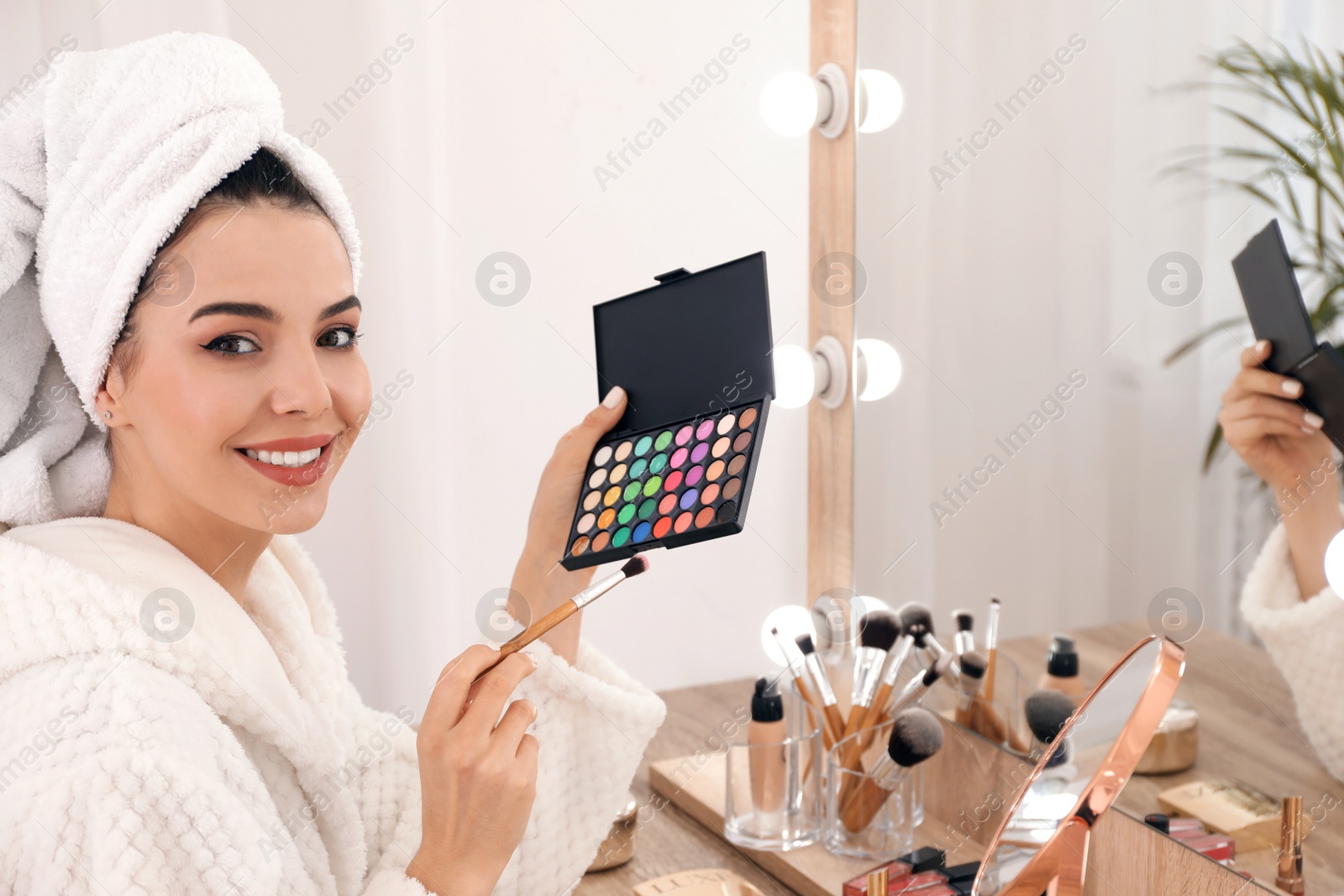 Photo of Beautiful woman applying makeup near mirror in room