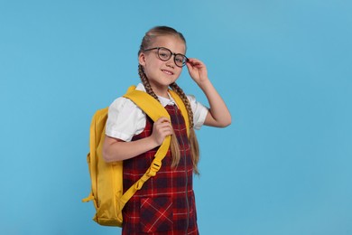 Happy schoolgirl in glasses with backpack on light blue background