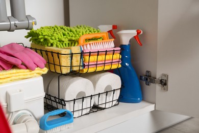 Photo of Open under sink cabinet with different cleaning supplies in kitchen