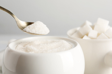 Photo of Taking spoon of white sugar from ceramic bowl on table, closeup