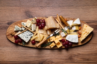 Photo of Cheese plate with rosemary, grapes and nuts on wooden table, top view
