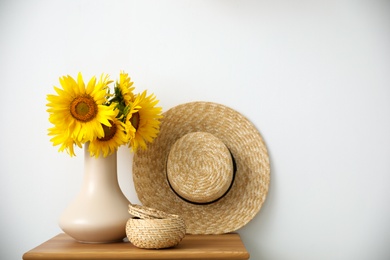 Photo of Bouquet of beautiful sunflowers, wicker basket and hat on table indoors