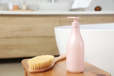 Photo of Bottle of shower gel and brush on wooden table near tub in bathroom, space for text