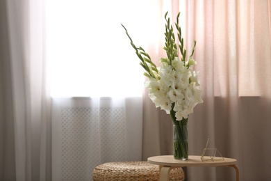 Vase with beautiful white gladiolus flowers on wooden table in room, space for text