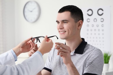 Photo of Vision testing. Ophthalmologist giving glasses to young man indoors