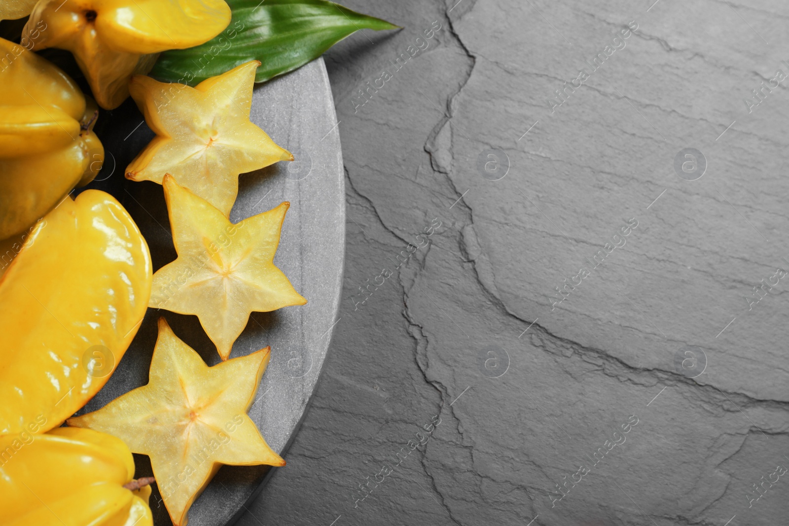 Photo of Cut and whole carambolas on black slate table, top view. Space for text