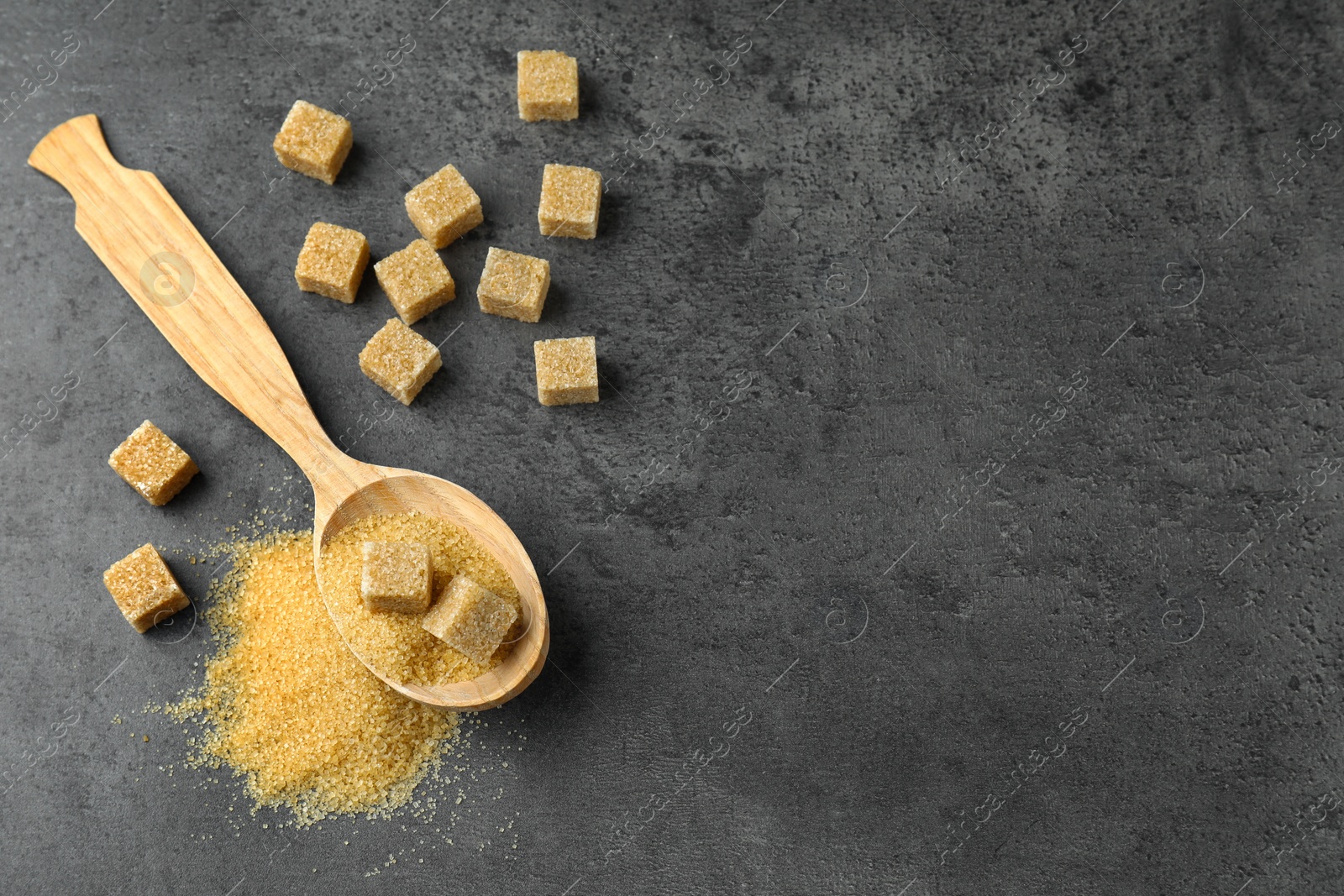 Photo of Spoon with brown sugar cubes on grey table, flat lay. Space for text