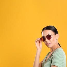 Beautiful woman wearing sunglasses on yellow background. Space for text