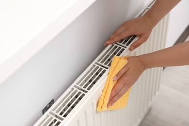 Photo of Woman cleaning radiator with rag indoors, closeup