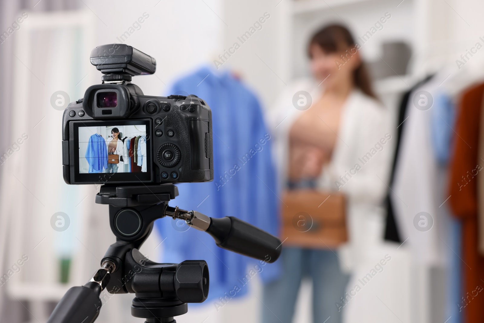 Photo of Fashion blogger showing her clothes while recording video at home, focus on camera